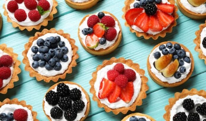 Many different berry tarts on blue wooden table, flat lay. Delicious pastries dessert